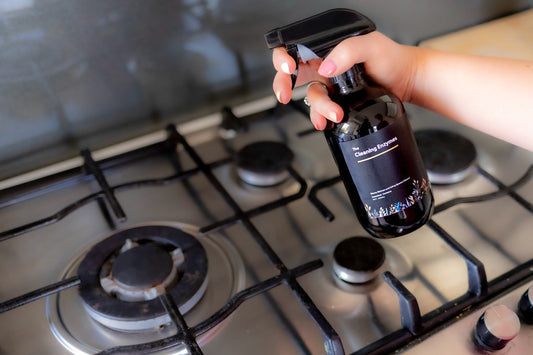 Hand spraying The Cleaning Enzymes Kitchen Rescue onto a gas stovetop